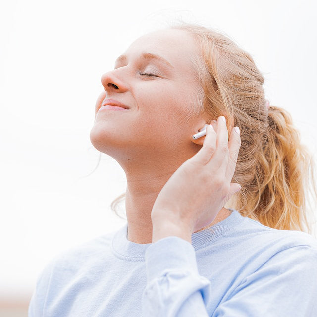 Woman with blonde hair in light blue sweater looking up with her hair to her ear wearing AirPods