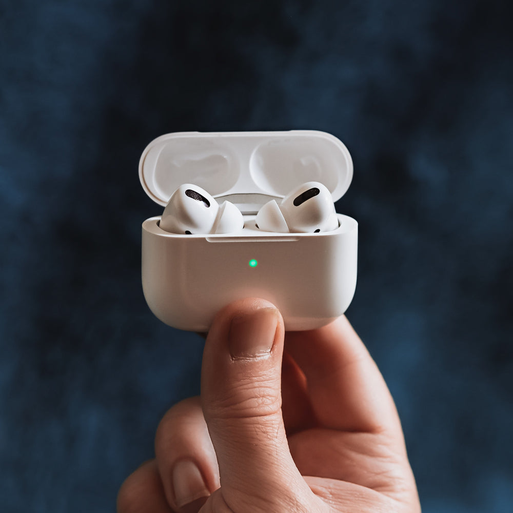 Hand holding Apple AirPods with a green LED light on the case