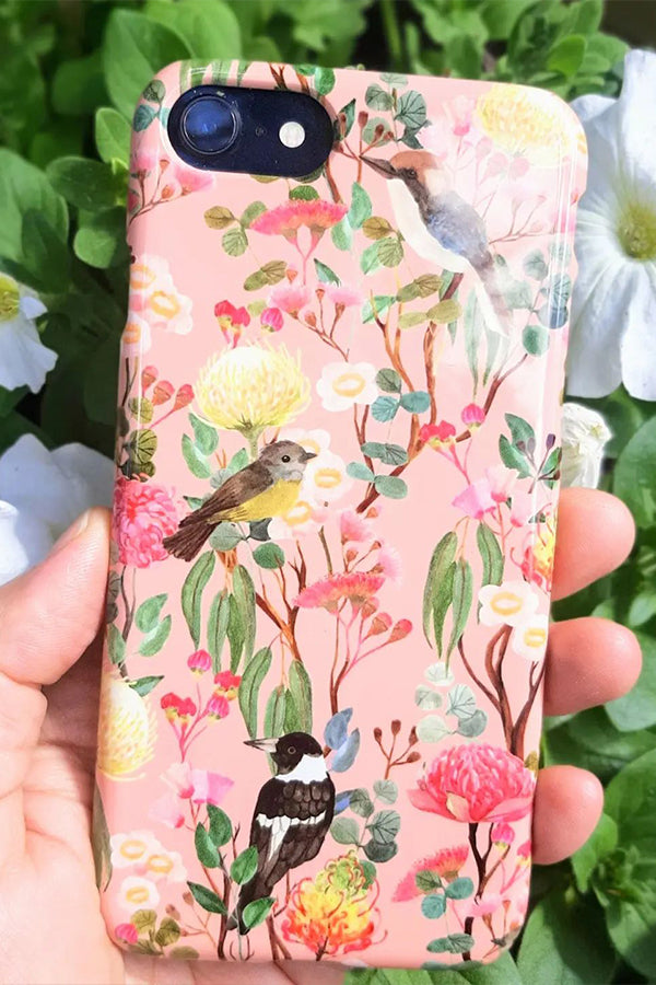 Phone case with floral and bird design held in front of greenery and flowers