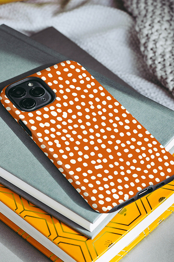 Orange phone case with a dotty pattern resting on some books