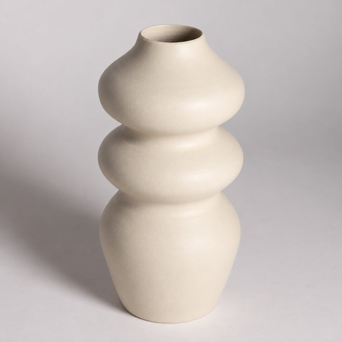 A modern, three-bulb-shaped ceramic vase in a matte cream finish, photographed against a neutral light gray studio background.