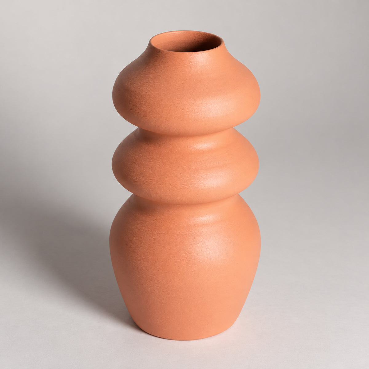 A terracotta-colored ceramic vase with a unique stacked, rounded organic shape, photographed against a neutral light gray background.