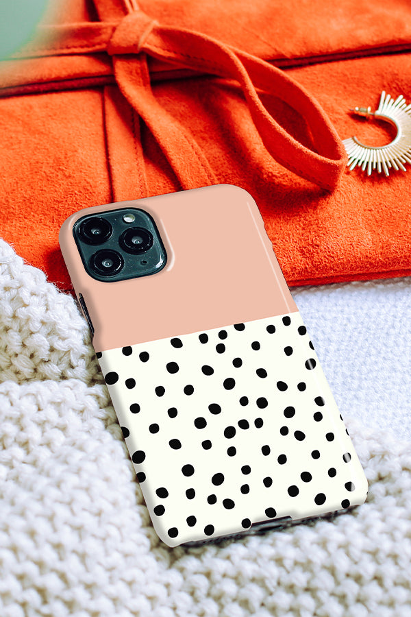 Phone case with a polka dot design on the bottom and a pink colour block on the top resting on a blanket