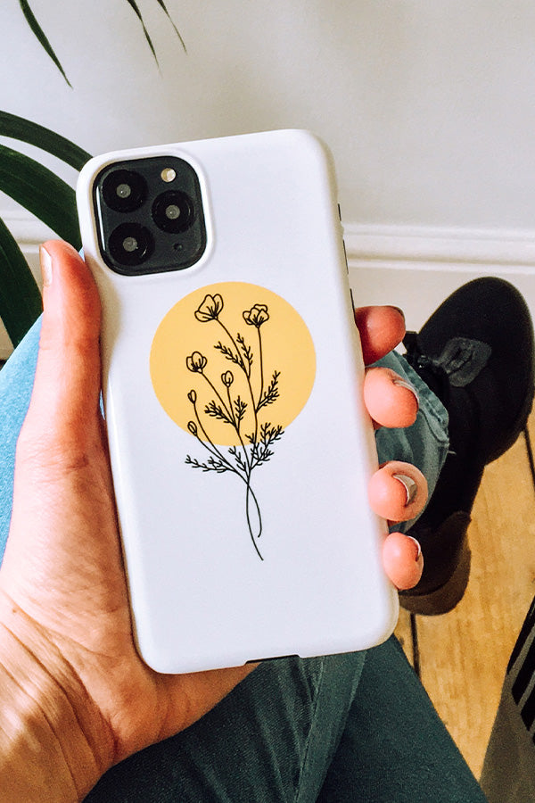 Phone case with a line art floral design with a yellow circle background held by a hand