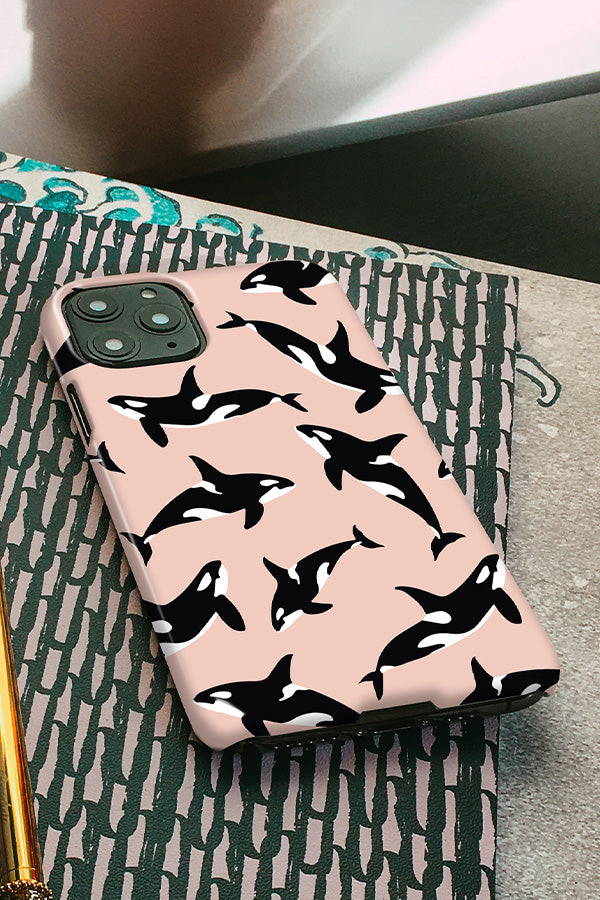 Phone case with a killer whale orca pattern on a pink background resting on a notebook