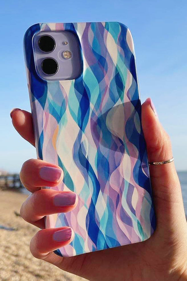 Phone case with wavy blue pattern held by a hand on a beach