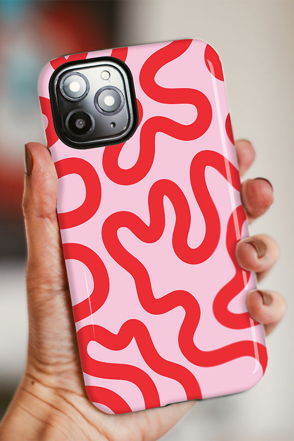 Phone case with red wavy pattern on a pink background held by a hand against a blurred background