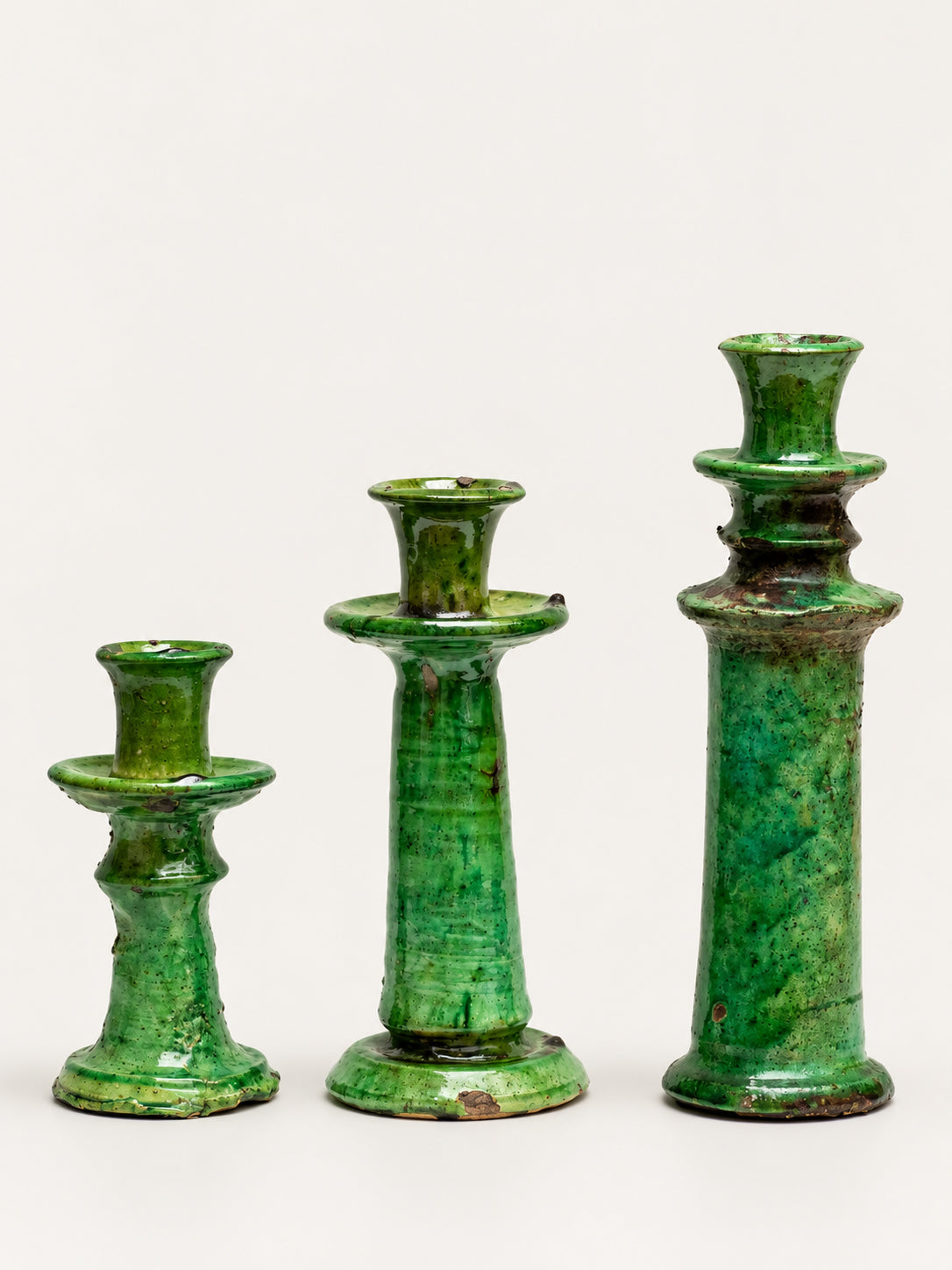 Three green glazed ceramic candlesticks of different heights arranged in ascending size order against a plain off-white background.