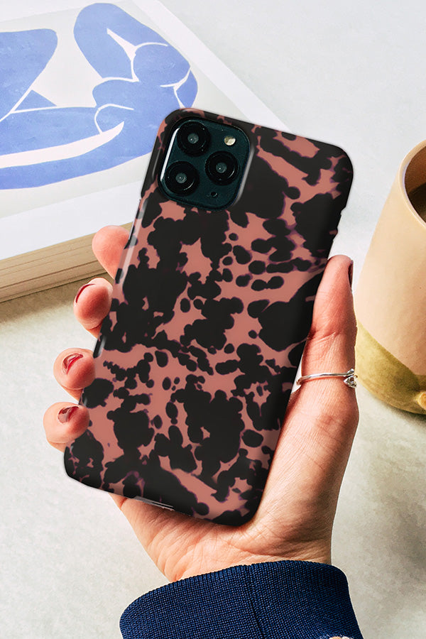 Hand holding a phone with a tortoise print design in black and peach pink