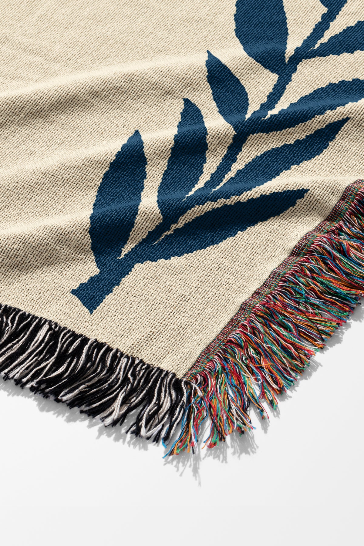 Beige blanket with blue leaf pattern and colorful fringe on a white background