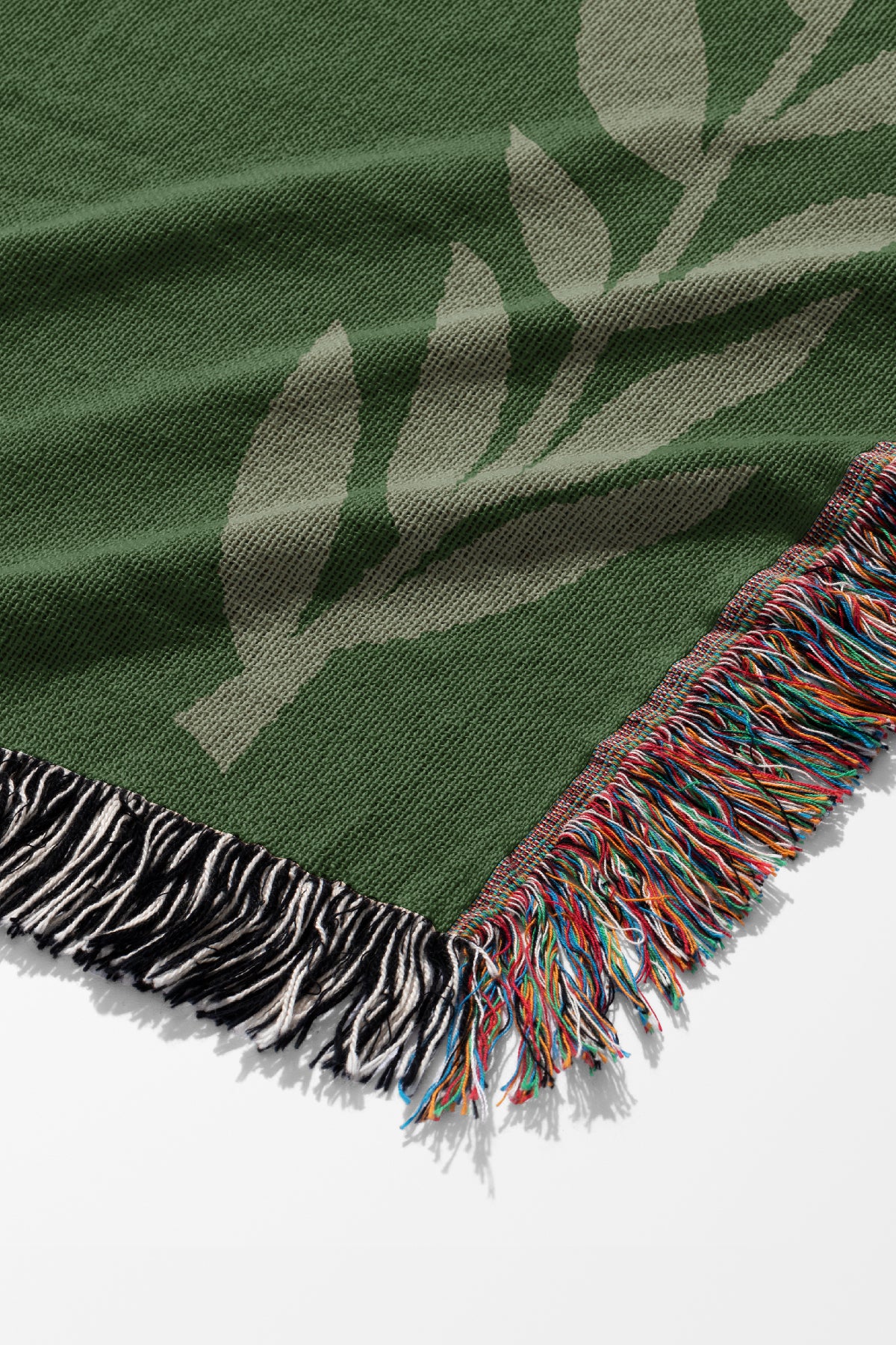 Green jacquard woven blanket close up with light green plants and colourful fringe