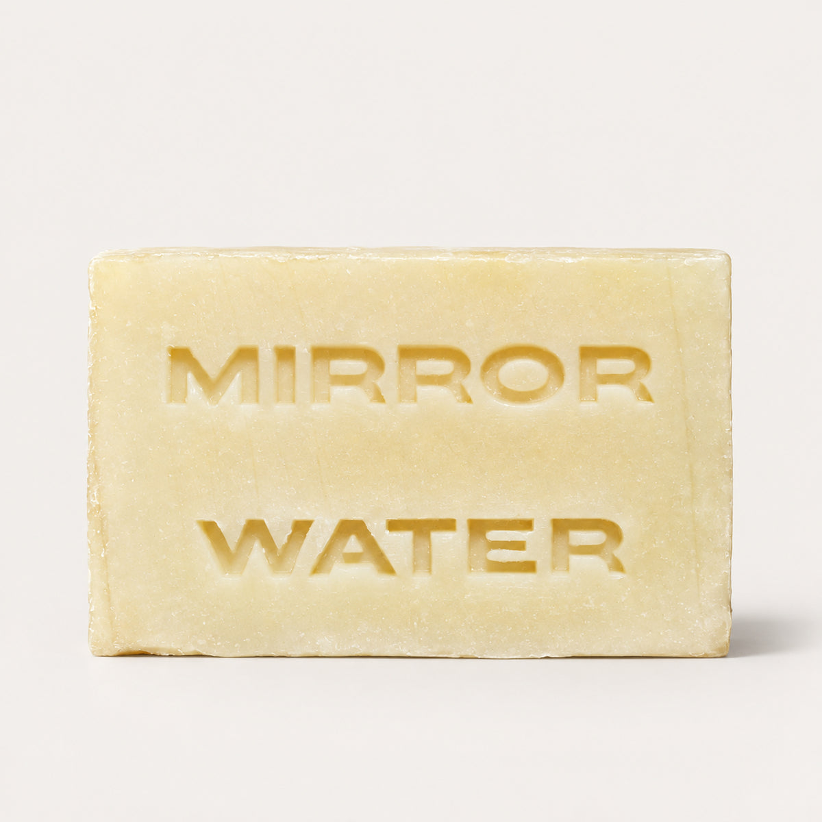 A rectangular pale yellow bar of soap with the words 'MIRROR WATER' embossed on the front, photographed against a clean off-white background.