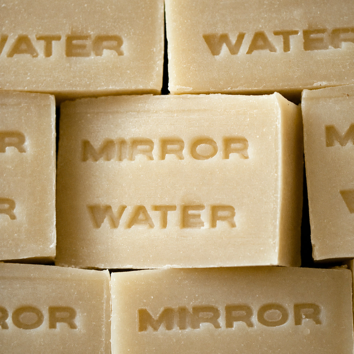 A close-up stack of pale beige rectangular soap bars embossed with the words 'MIRROR WATER'.