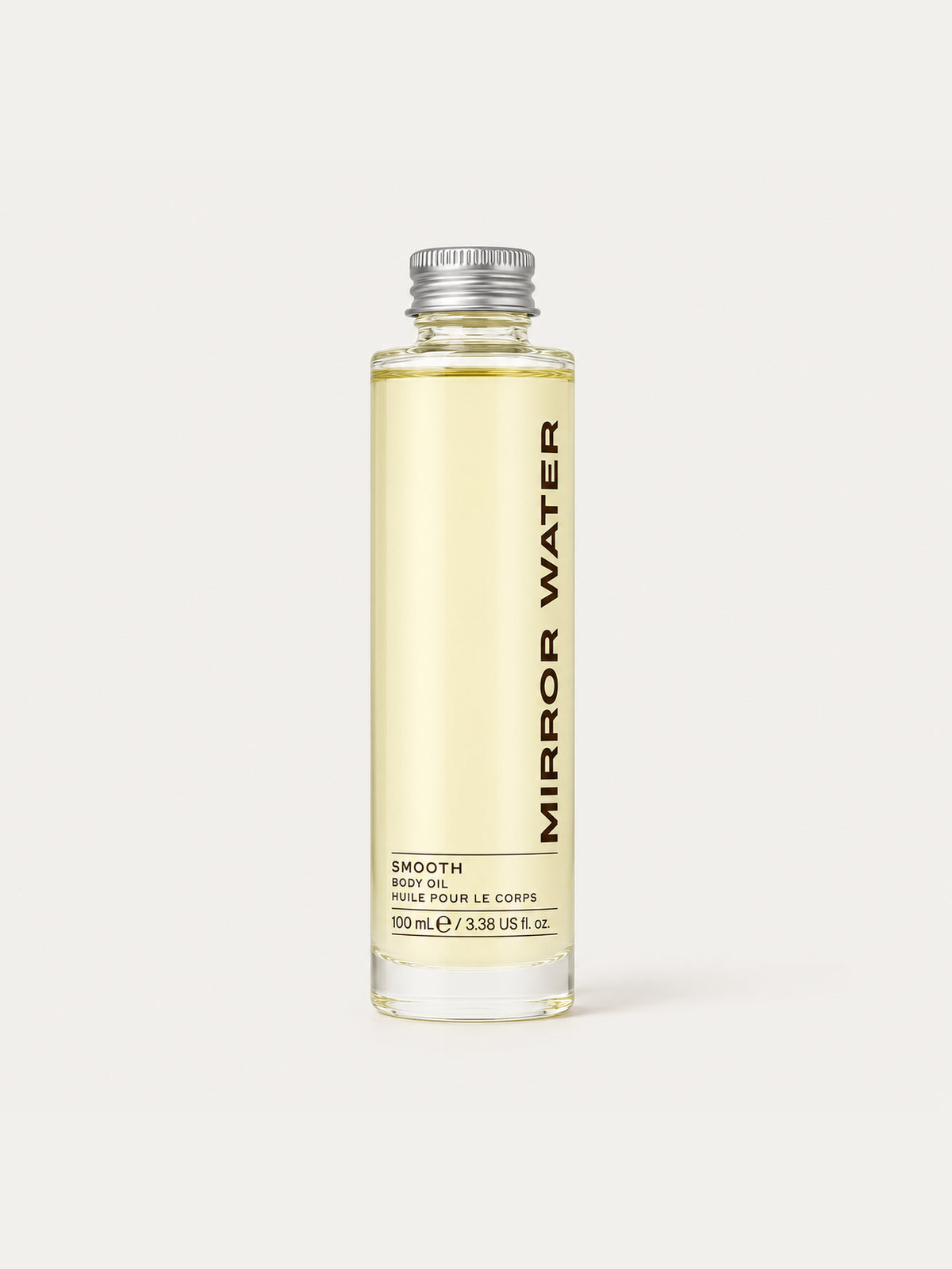 A clear glass bottle of Mirror Water Smooth Body Oil with a silver cap, filled with pale yellow oil, set against a solid off-white background.