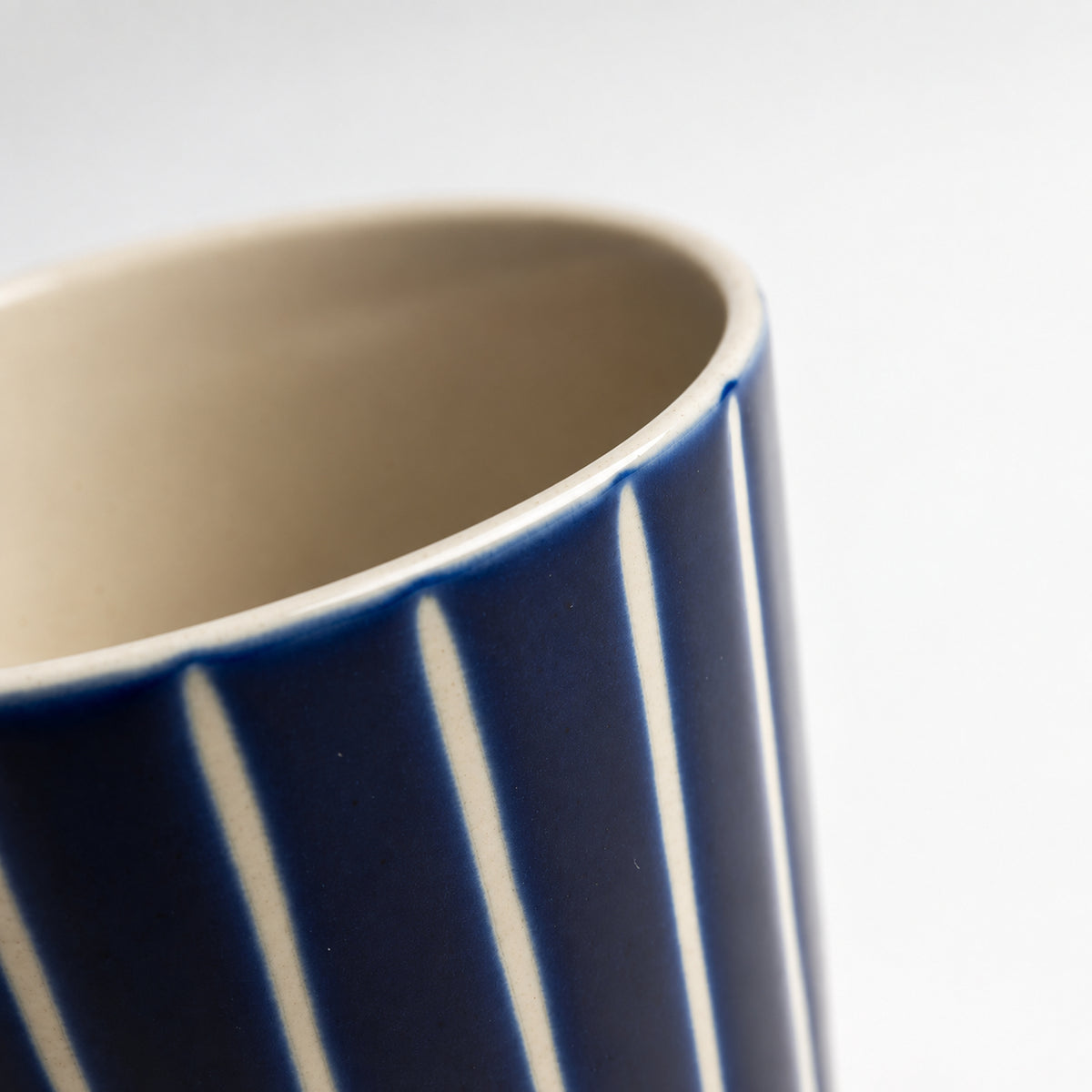 Close-up of a ceramic mug showing a deep navy blue exterior with vertical white stripes and a warm cream-colored interior, set against a plain light gray background.